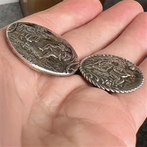 Two silver buttons of people in nature.