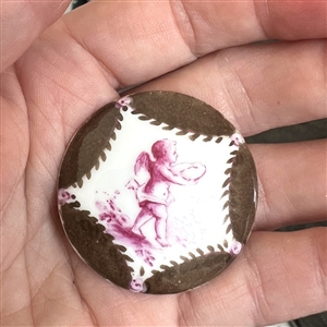 Painted porcelain button of a cherub/putti offering a gift.