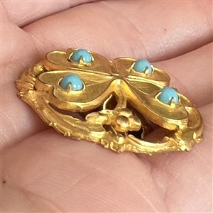 Brass button of a four leaf clover with turquoise glass.