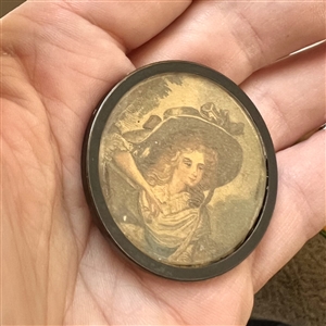 Printed fabric under glass button of a woman in a huge hat.