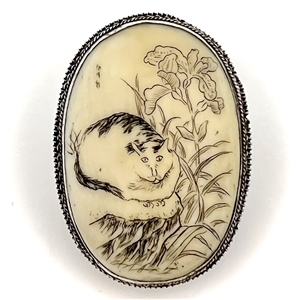 Incised and inked natural material button of a cat and plant life.