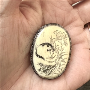 Incised and inked natural material button of a cat and plant life.