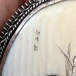 Incised and inked natural material button of a cat and plant life.