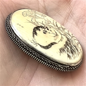 Incised and inked natural material button of a cat and plant life.
