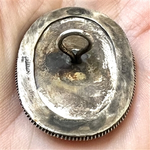 Incised and inked natural material button of a cat and plant life.