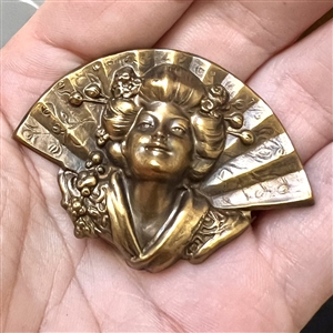 Stamped brass in high relief button of a realistic fan behind a Asian woman.
