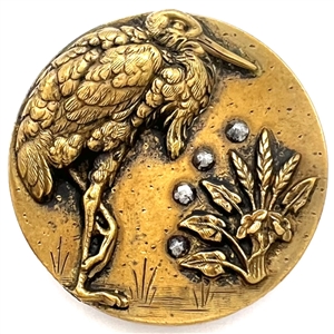 Brass button of a heron standing on one leg.